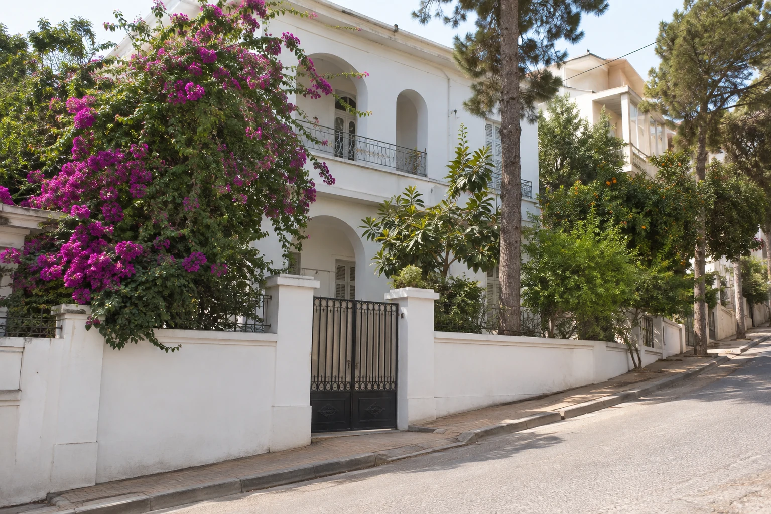 Weiße Villa mit Gartenmauer und grüner Bepflanzung an einer Straße in El Mouradia